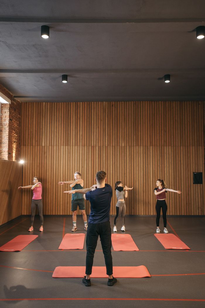 team-03 A diverse group of adults stretching together in an indoor fitness class, led by an instructor.